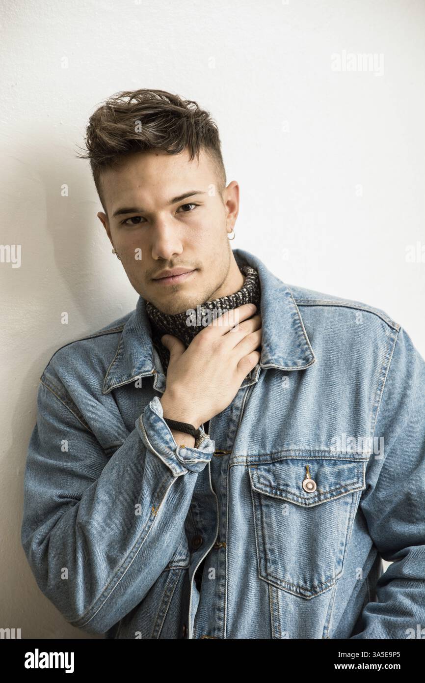 Bel giovane asiatico bianco che indossa una giacca blu in denim che tiene il collo a causa del mal di gola, in piedi su uno sfondo chiaro contro il muro in uno studio Foto Stock