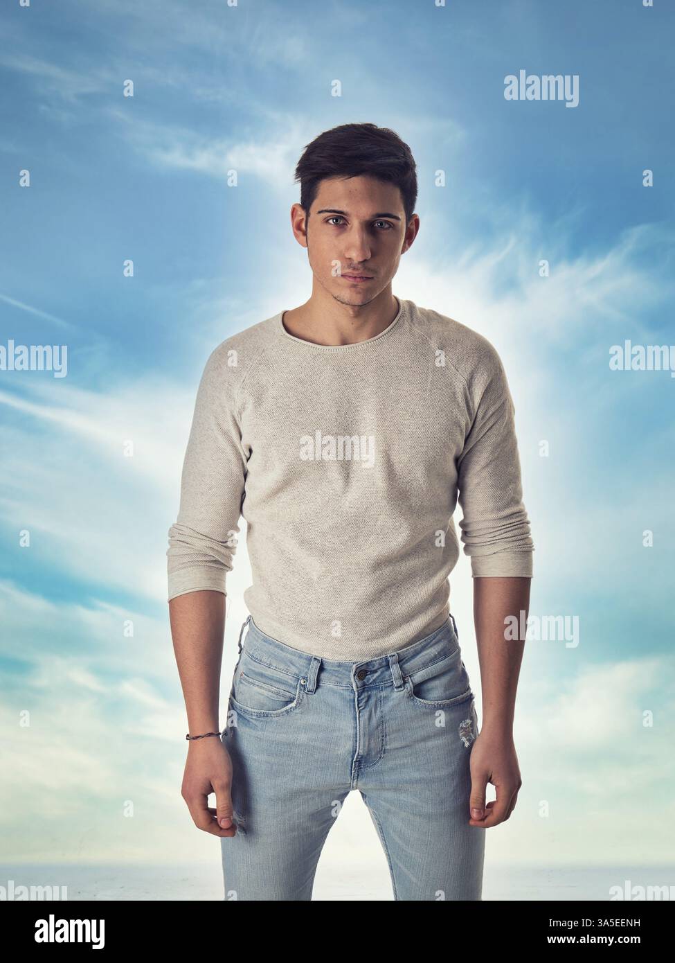 Un giovane attraente che si erge contro il cielo blu, guarda lo spettatore e guarda la telecamera con grande serietà Foto Stock