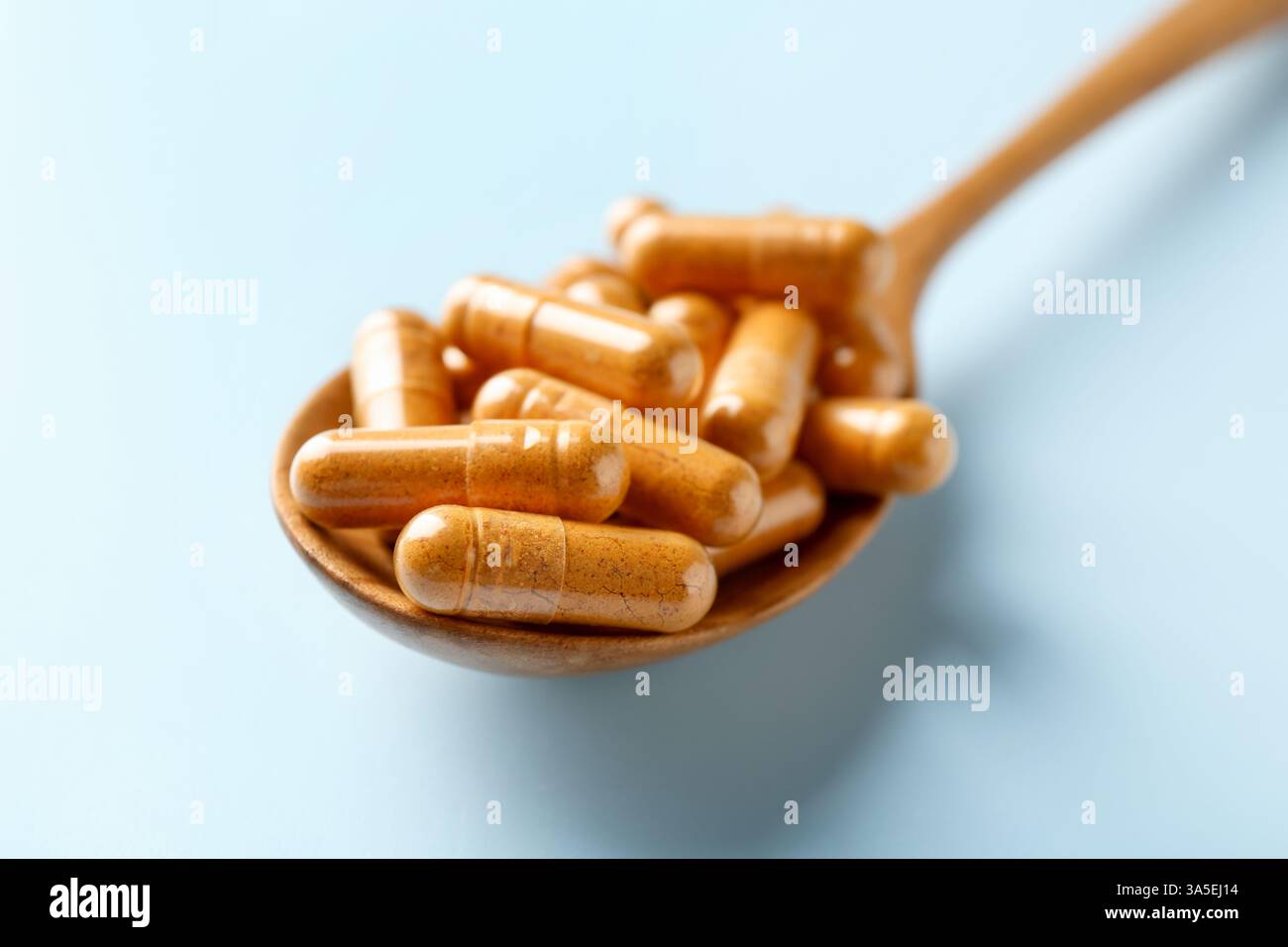 Capsule di curcuma in cucchiaio di legno su sfondo azzurro, primo piano Foto Stock