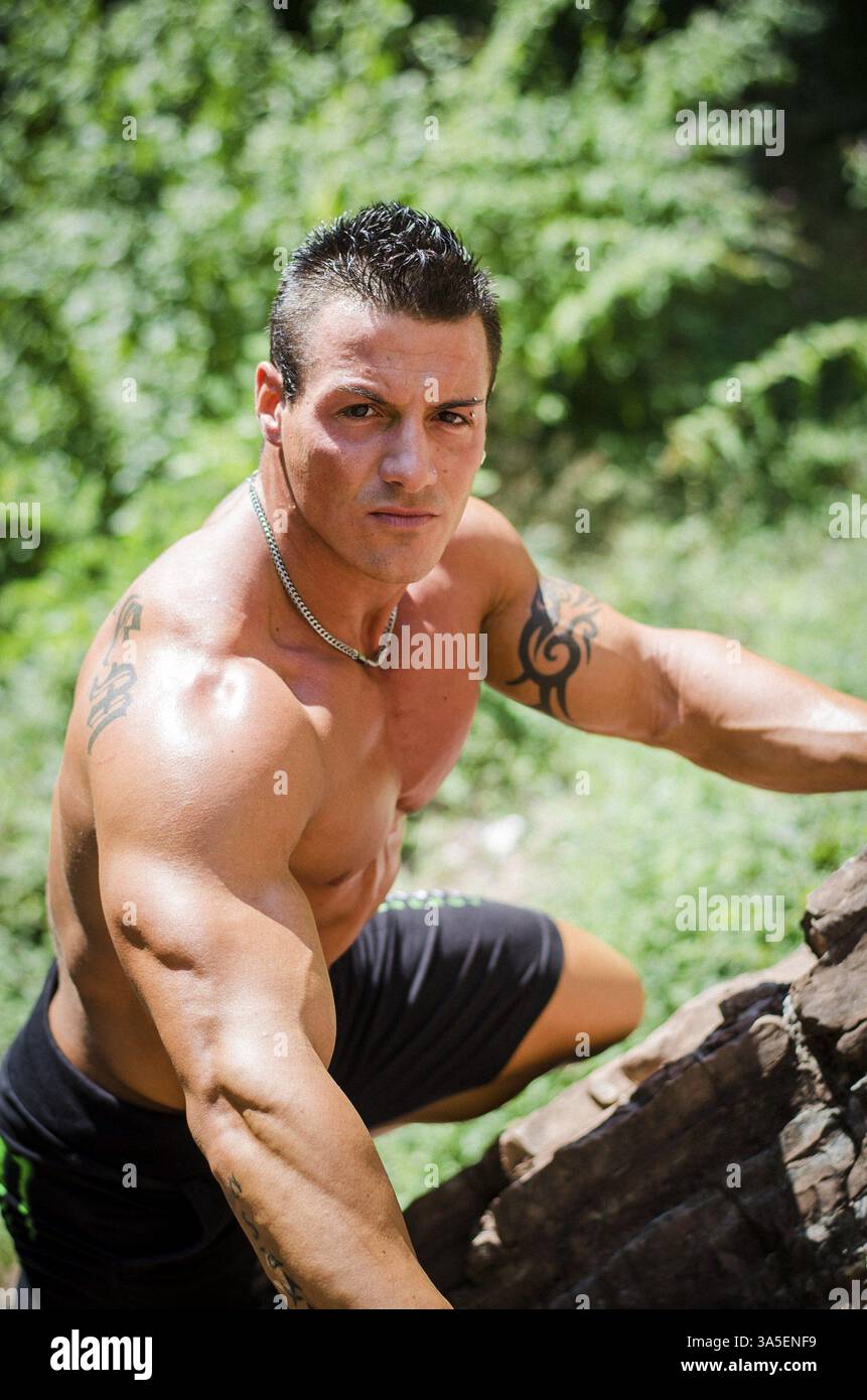 Bello, muscolare, shirless scalatore, cercando nella fotocamera e arrampicata parete di pietra Foto Stock