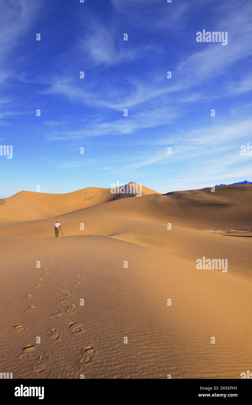 Alba nelle sabbie arancioni del deserto di Mesquite Flat, Stati Uniti. Donna - la fotografa con una maglietta a righe è pronta a scattare con un treppiede tra la sabbia Foto Stock