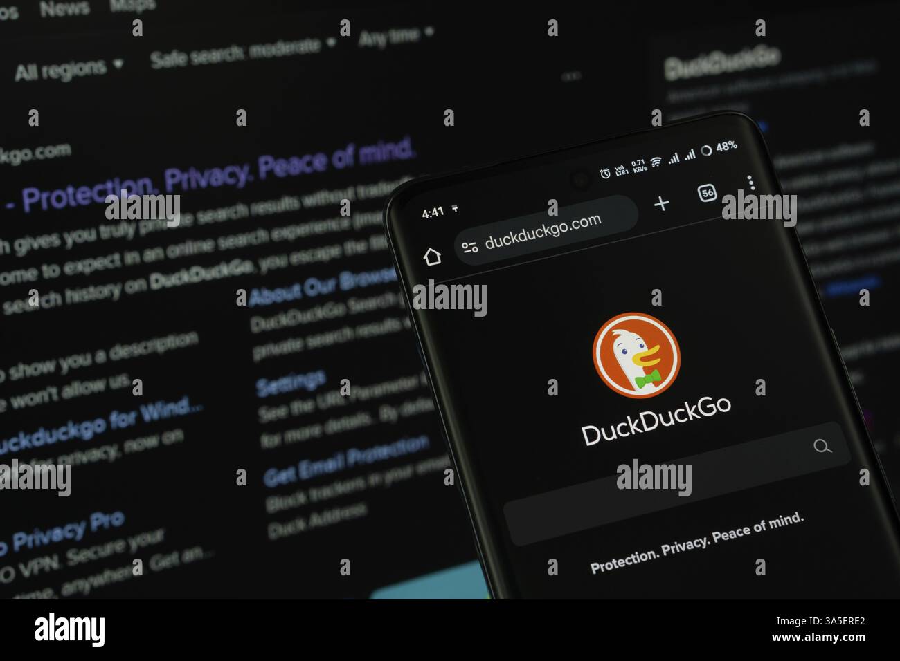 L'app di DuckDuckGo viene visualizzata sullo schermo di uno smartphone e il sito Web DuckDuckGo è visibile sullo schermo di un computer sullo sfondo Foto Stock
