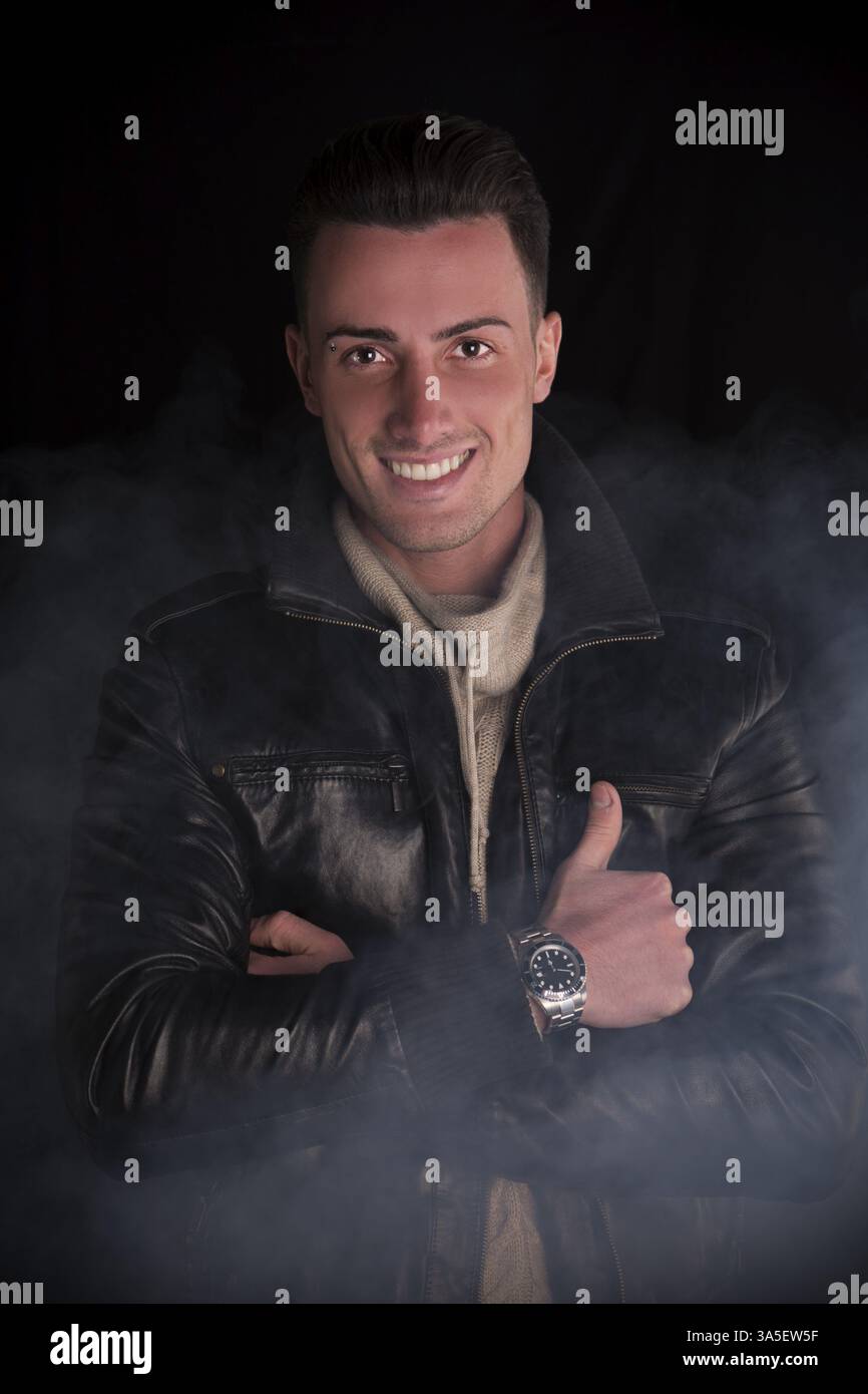 Attraente giovane con maglione bianco e nero giacca di pelle. Fumo e sfondo scuro Foto Stock