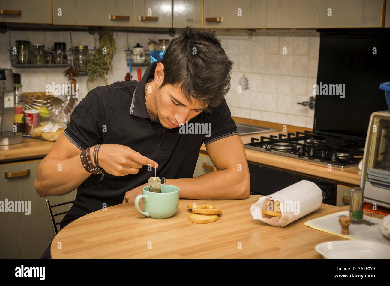 Stanchi o malati attraente Giovane Uomo appoggiato con il gomito sul tavolo di cucina e tenendo tazza di caffè per la prima colazione Foto Stock