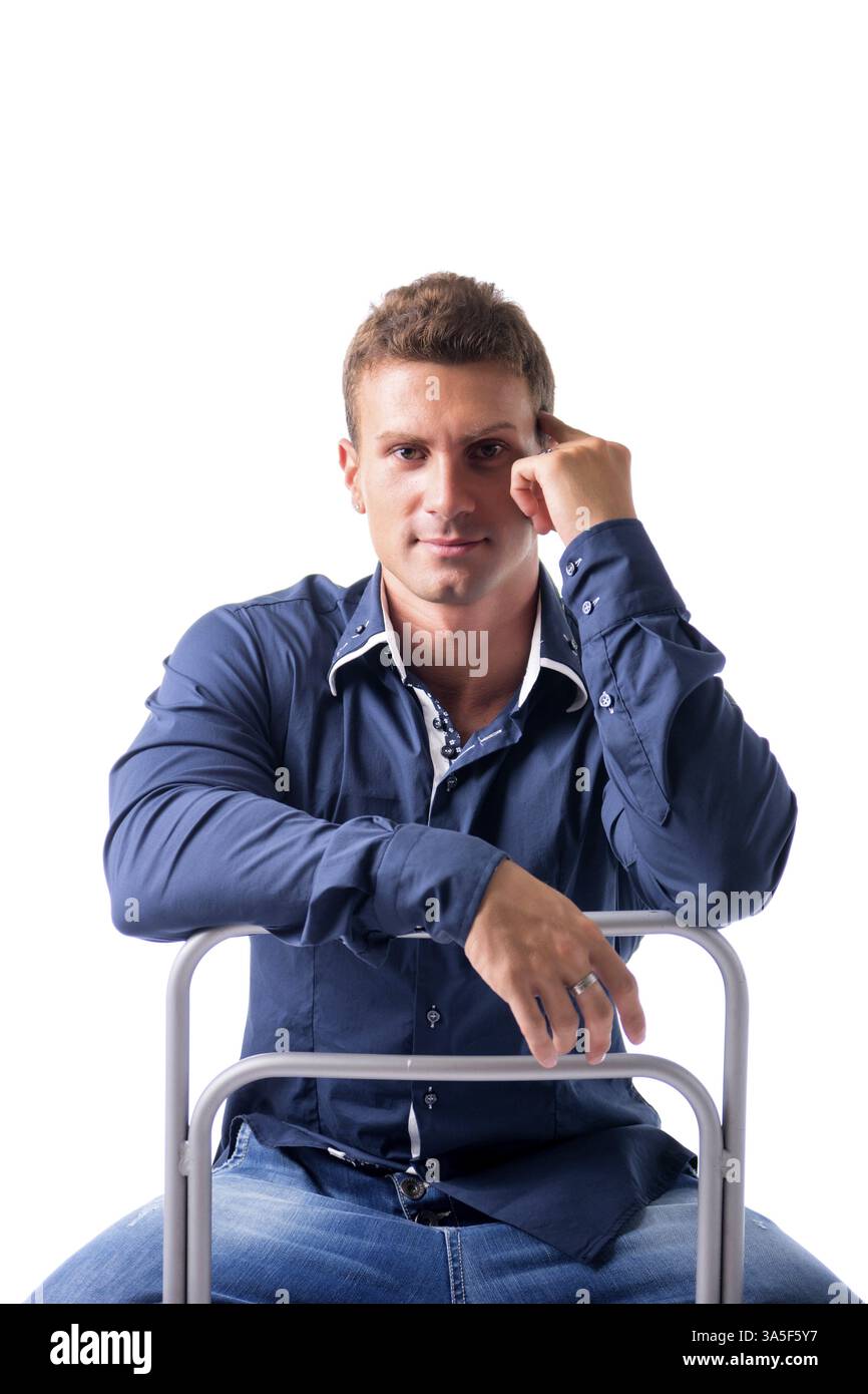 Attraente giovane uomo seduto, appoggiata sul retro di una sedia e guardando la telecamera, isolato su bianco Foto Stock