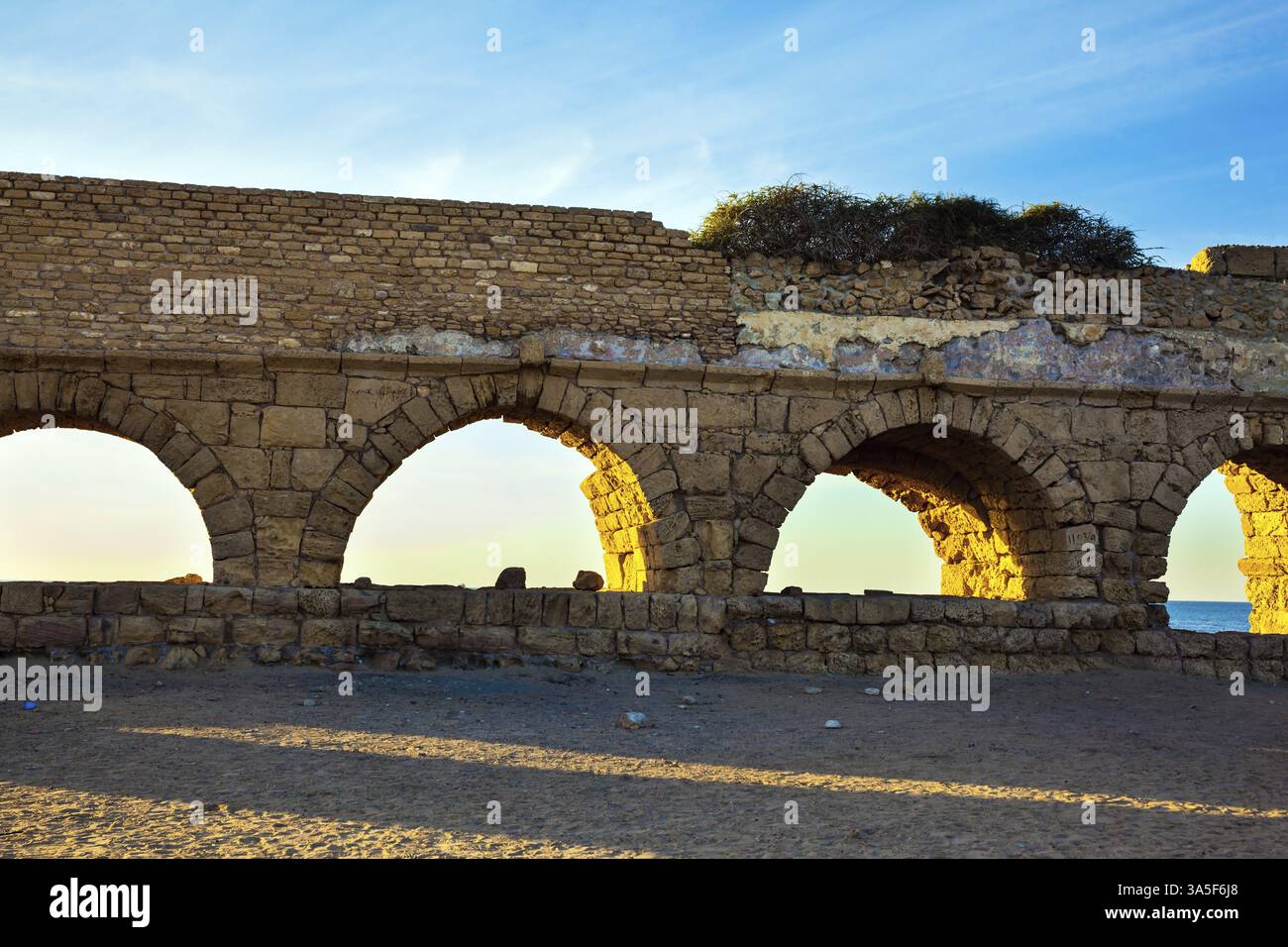 Tramonto magico a Caesarea. L'antico acquedotto romano è illuminato dal sole del tramonto. Le lunghe ombre serali giacciono uniformemente sulla sabbia calda Foto Stock