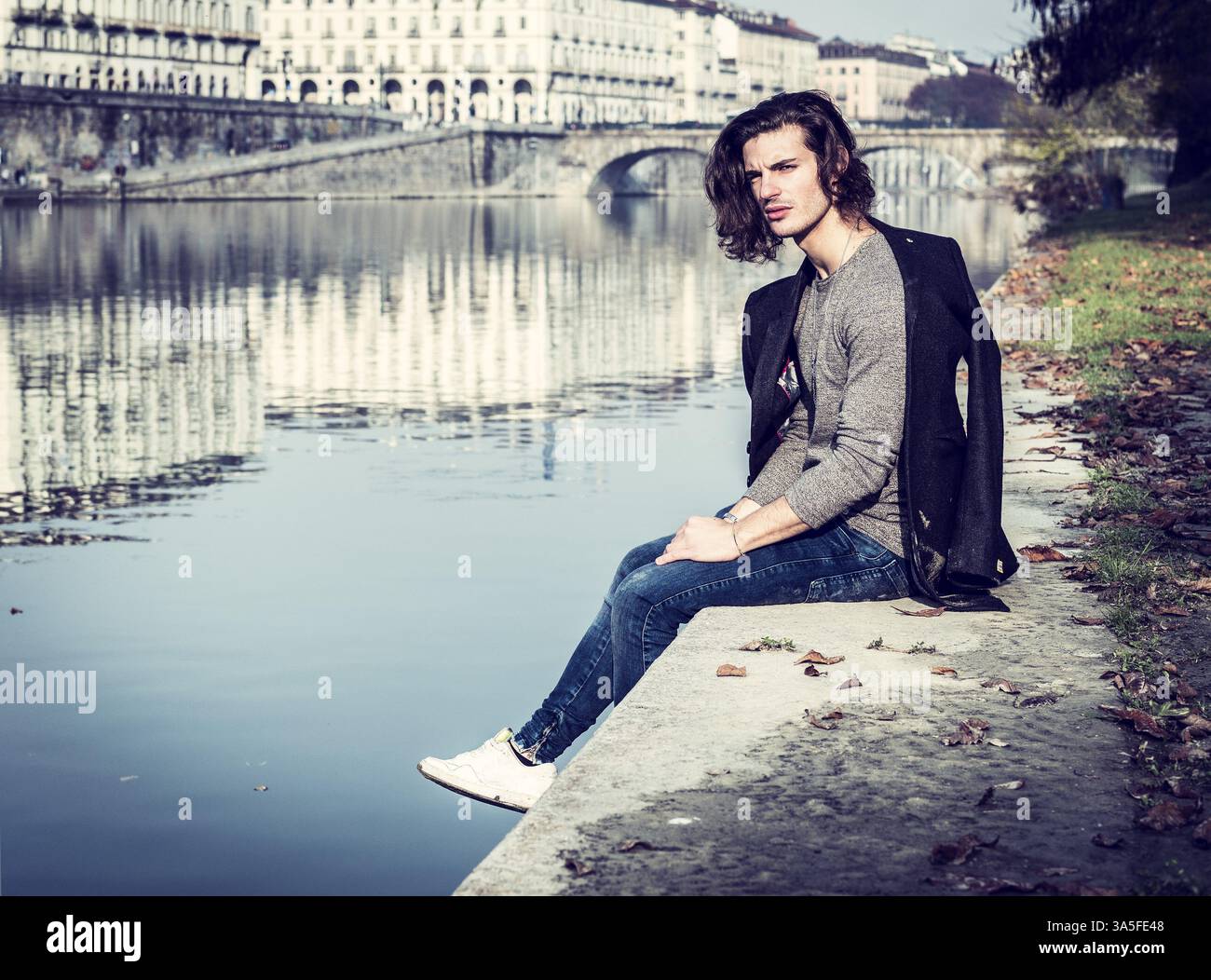 Un bel giovane uomo nel contesto urbano in città europea, Torino in Italia seduta sulle sponde del fiume Po, nella fredda giornata invernale Foto Stock