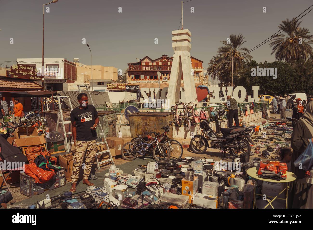 Una strada trafficata nel mercato del centro di Douz, Tunisia, piena di biciclette, motociclette, officine di riparazione, e vivace attività locale Foto Stock
