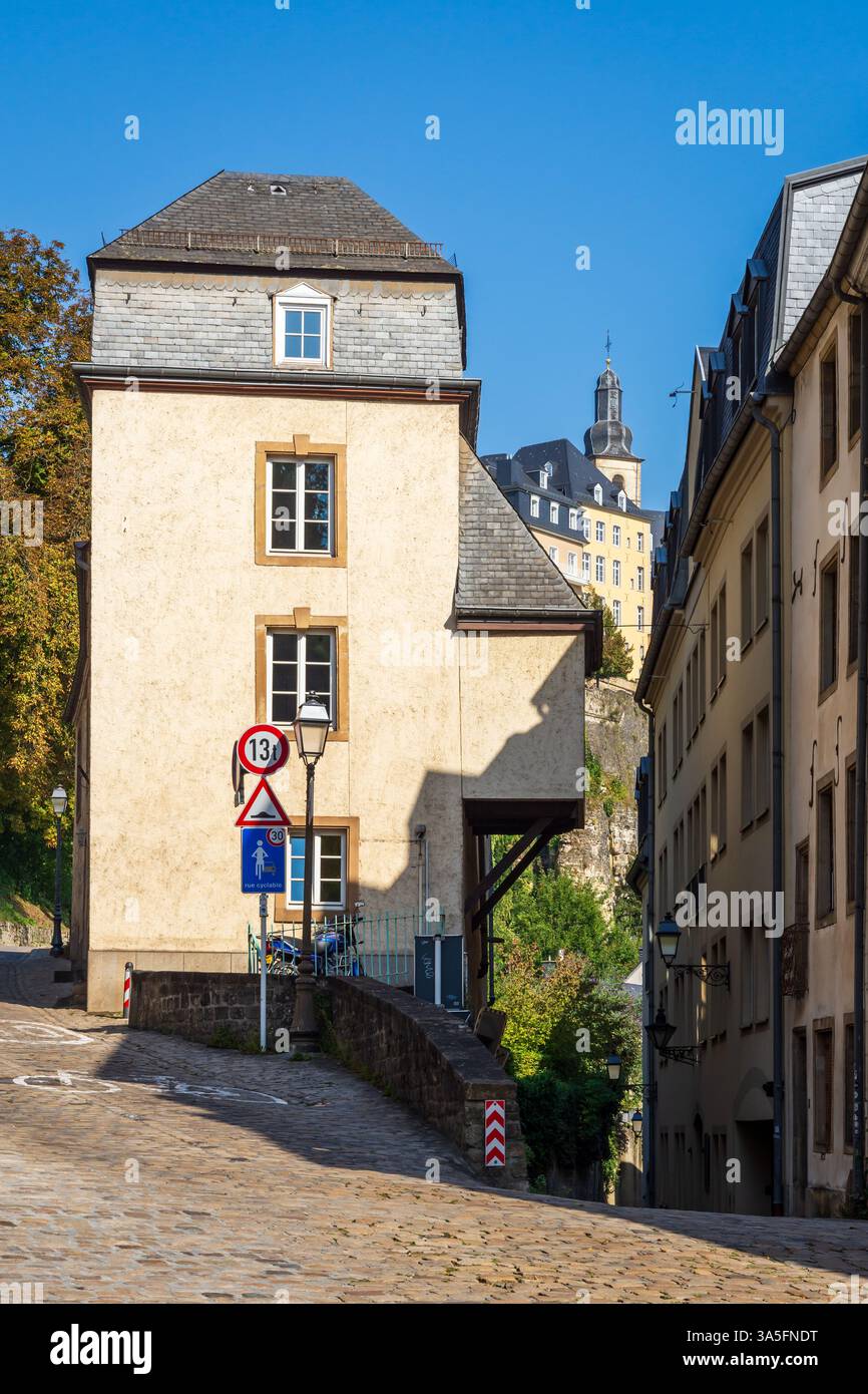 Un'antica casa cittadina in una strada acciottolata nel quartiere Grund a Lussemburgo, con il campanile della chiesa di San Michele in lontananza Foto Stock