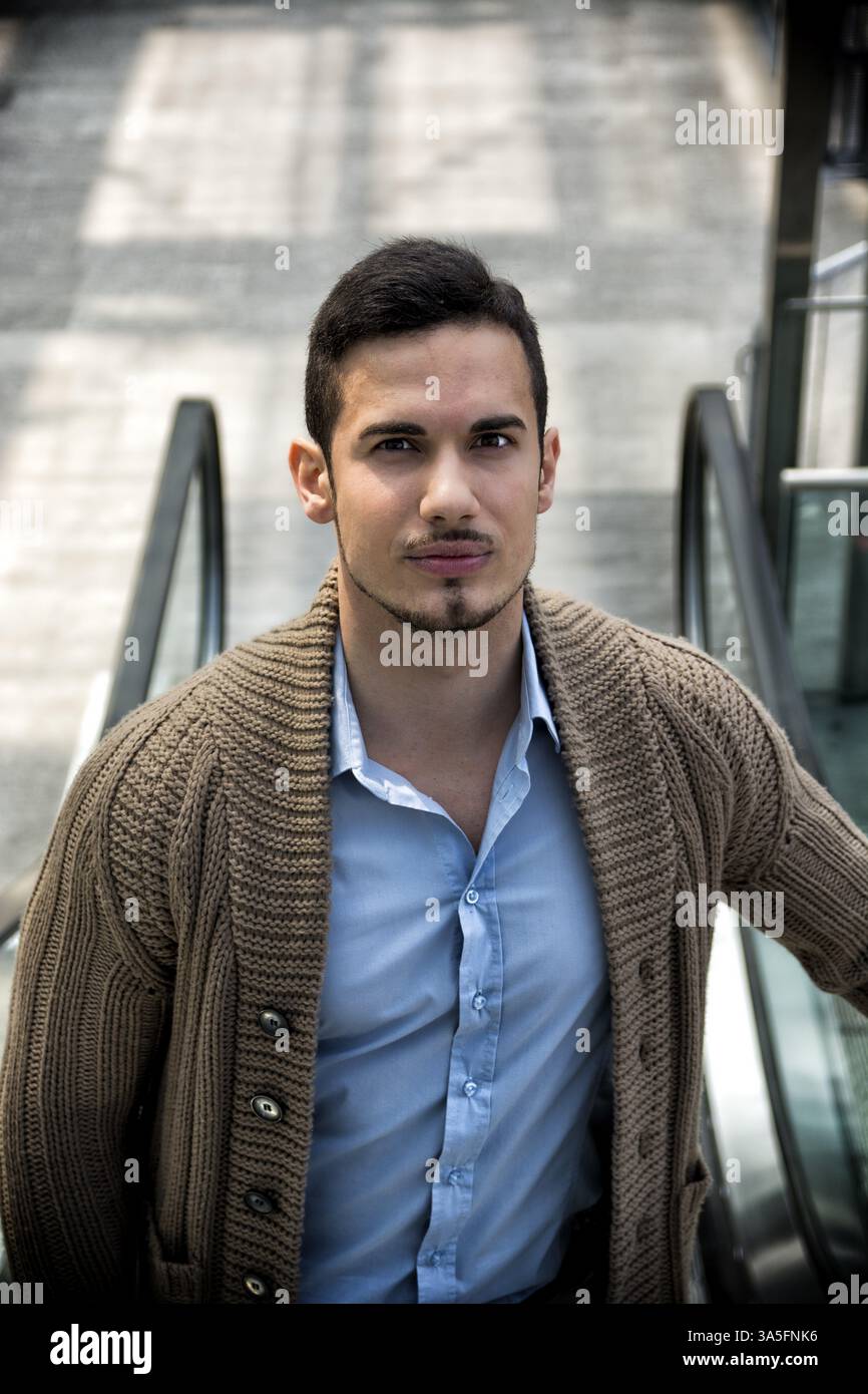 Ritratto di attraente giovane uomo su scale mobili, guardando la fotocamera Foto Stock