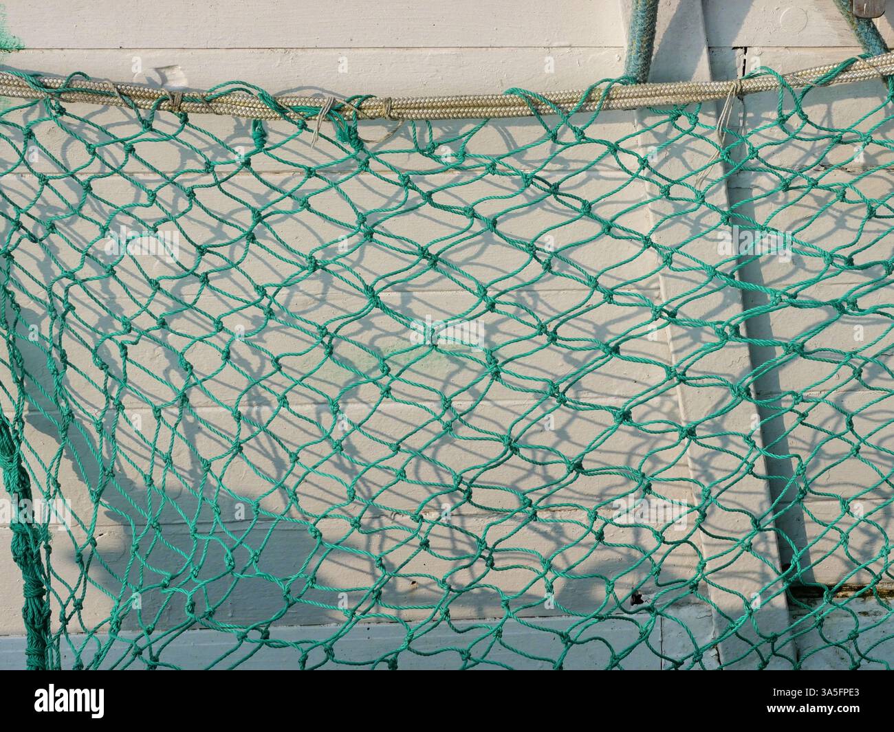 Rete protettiva sul lato di un'imbarcazione. Una rete protettiva verde sulla barca da pesca crea una struttura emozionante con la sua ombra sul lato della nave. Foto Stock