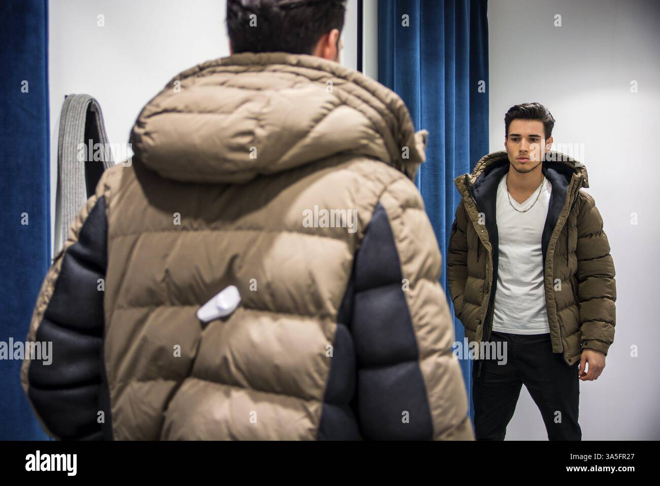 Giovane uomo bello che prova i vestiti nel negozio di abbigliamento&#39, spogliatoio davanti a uno specchio o all'armadio in camera Foto Stock