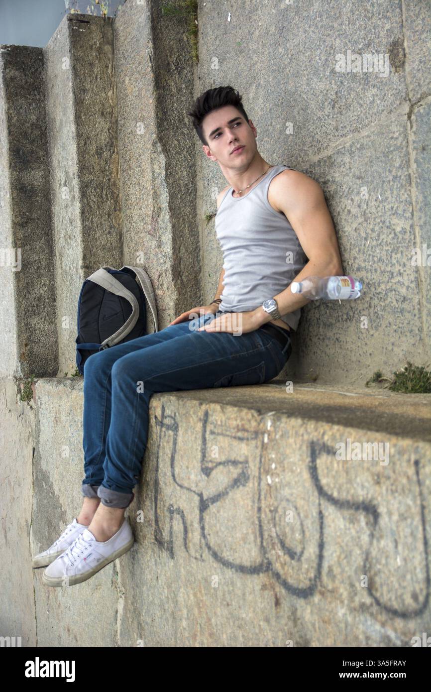 Giovane uomo con zaino e acqua in bottiglia giacente a terra vicino alla scala - Trick, Impossible Illusion, immagine ruotata per apparire come se l'uomo fosse seduto su Foto Stock