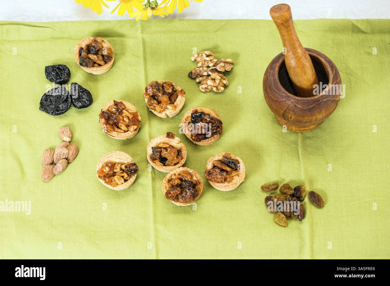 Cottura professionale. Cestini di pasta frolla in porzioni con ripieno di frutta secca e frutta secca. Mortaio in legno di fondo con pestello Foto Stock