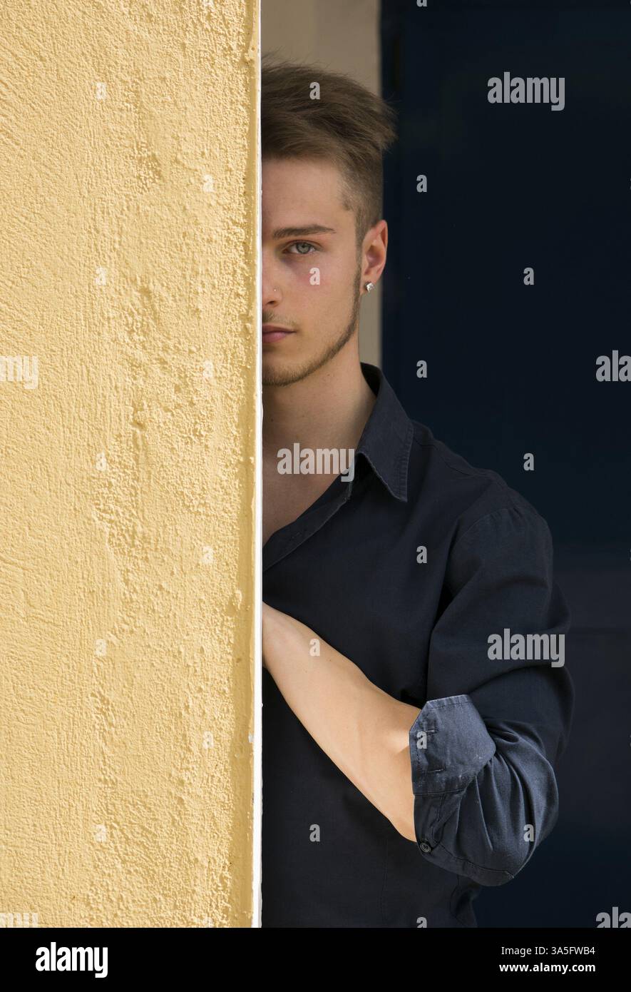 Bella bionda giovane nasconde metà faccia dietro la parete guardando la fotocamera con un occhio Foto Stock