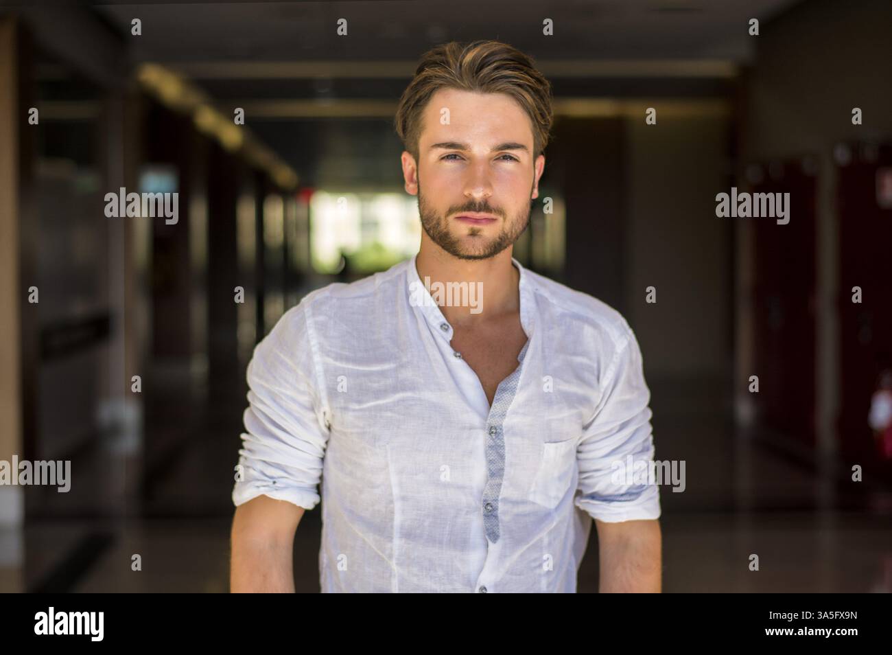 Vita Ritratto di giovane attraente uomo maglietta indossa in piedi che guarda pensieroso nei corridoi della scuola o centro commerciale per lo Shopping Foto Stock