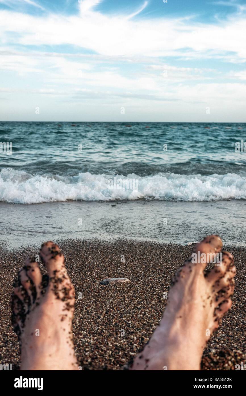 I piedi di un uomo sdraiato su una spiaggia sabbiosa vicino al mare. Foto Stock