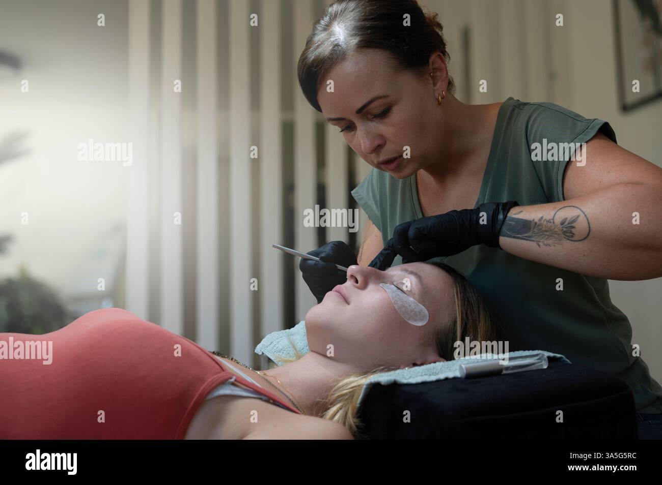 Primo piano di bellezza di una giovane donna che si solleva la ciglia con un sollevamento ciglia da parte di un estetista in un salone di bellezza. Dare forma alle sopracciglia. Foto Stock