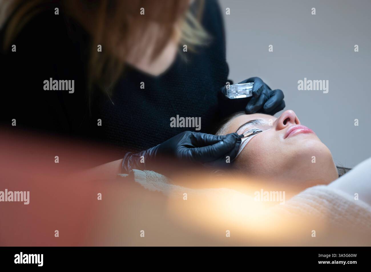 Primo piano di bellezza di una giovane donna che si solleva la ciglia con un sollevamento ciglia da parte di un estetista in un salone di bellezza. Dare forma alle sopracciglia. Foto Stock