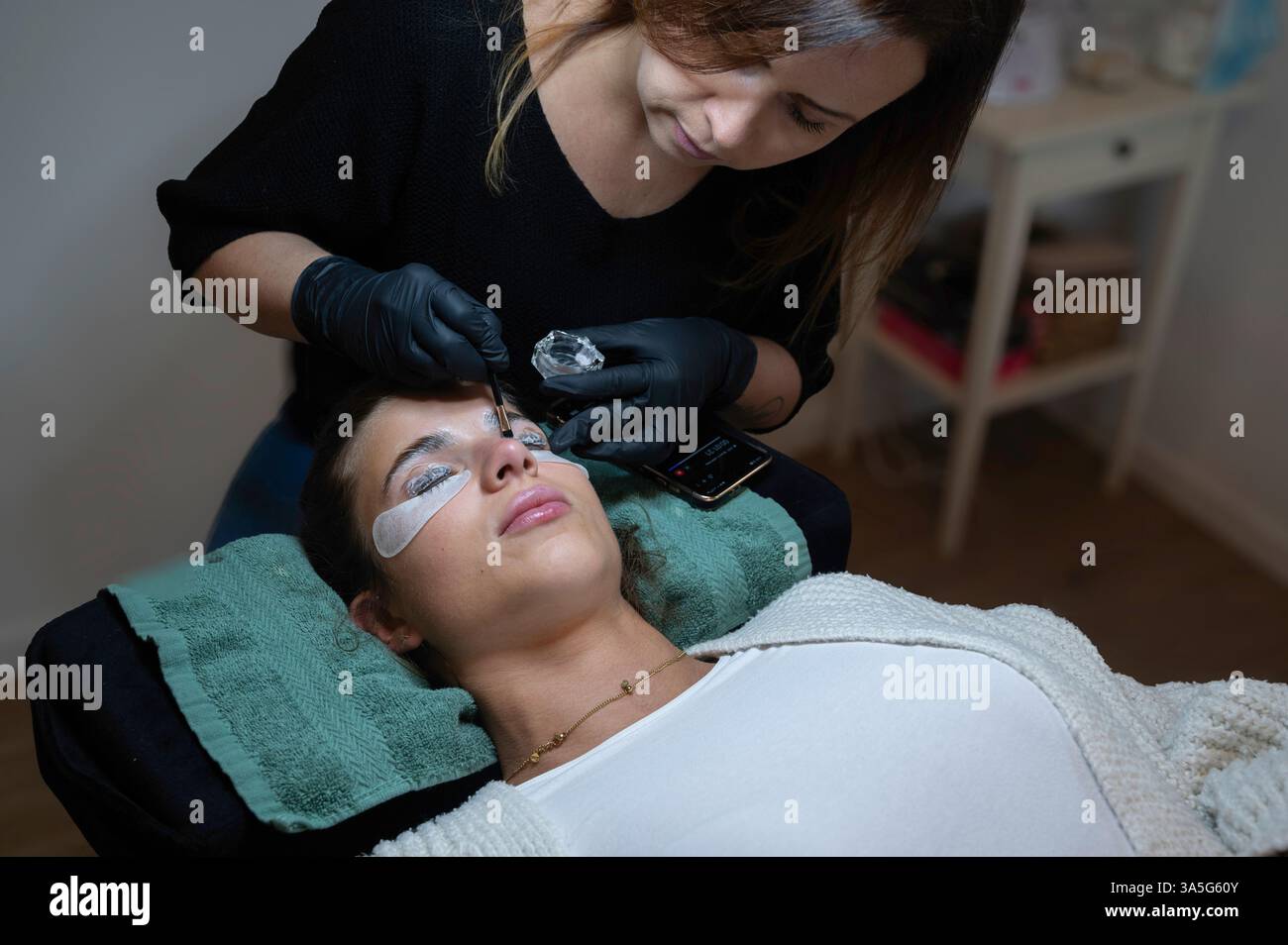 Primo piano di bellezza di una giovane donna che si solleva la ciglia con un sollevamento ciglia da parte di un estetista in un salone di bellezza. Dare forma alle sopracciglia. Foto Stock