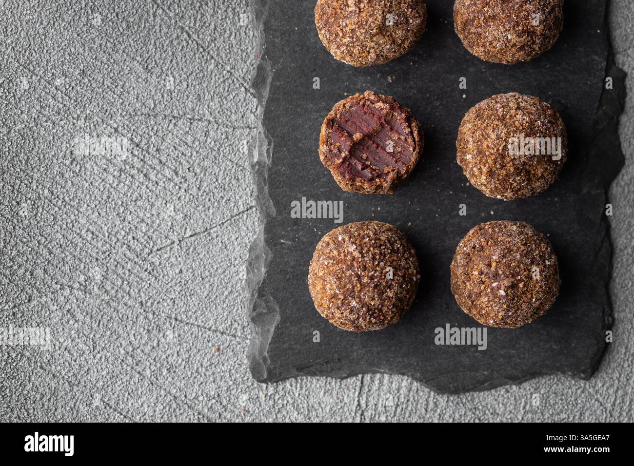 Caramelle artigianali al tartufo al cioccolato con ripieno di frutti di bosco e frutta su sfondo scuro, bonbon fatti a mano o artigianali, cioccolato o conce dolciarie Foto Stock