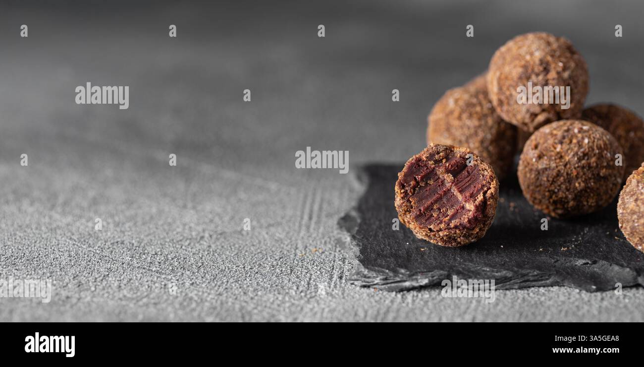 Caramelle artigianali al tartufo al cioccolato con ripieno di frutti di bosco e frutta su sfondo scuro, bonbon fatti a mano o artigianali, cioccolato o conce dolciarie Foto Stock