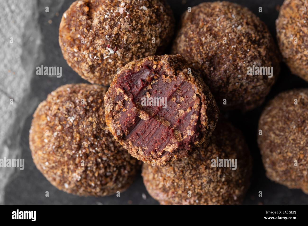 Caramelle artigianali al tartufo al cioccolato con ripieno di frutti di bosco e frutta su sfondo scuro, bonbon fatti a mano o artigianali, cioccolato o conce dolciarie Foto Stock