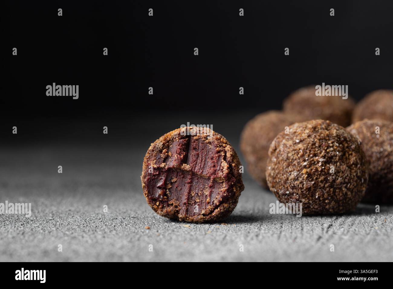 Caramelle artigianali al tartufo al cioccolato con ripieno di frutti di bosco e frutta su sfondo scuro, bonbon fatti a mano o artigianali, cioccolato o conce dolciarie Foto Stock