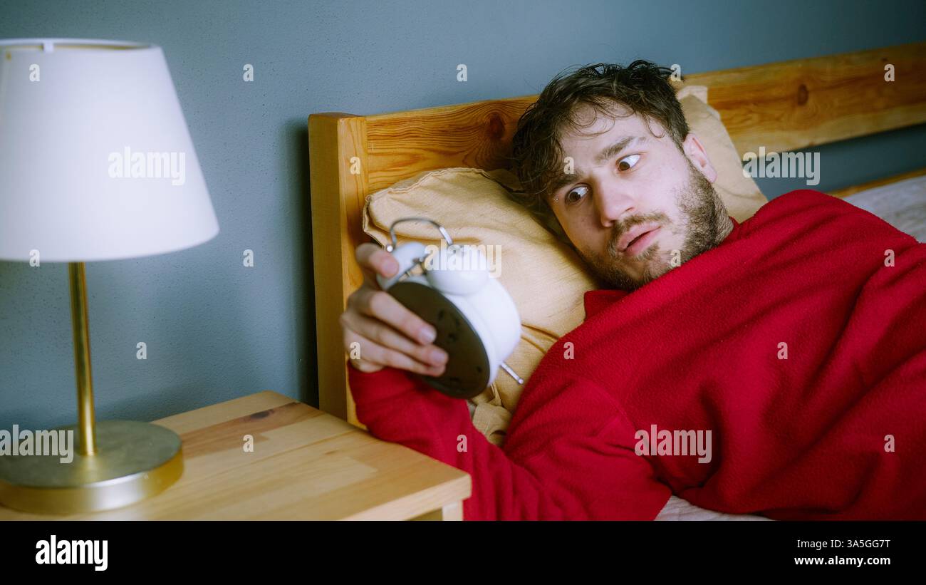 Giovane che lotta per svegliarsi, colpendo Snooze alla sveglia Foto Stock