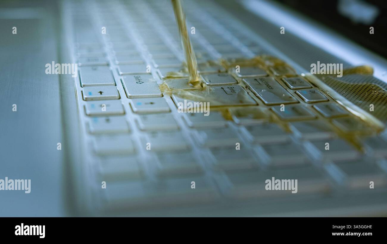 Il tè versato sulla tastiera del laptop causa danni e malfunzionamenti, incidente con liquidi sul dispositivo elettronico, primo piano dei tasti del computer bagnato Foto Stock
