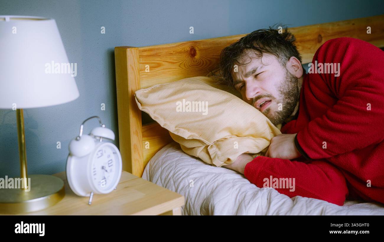 Giovane uomo che lotta per svegliarsi – guardare Snooze alla sveglia Foto Stock