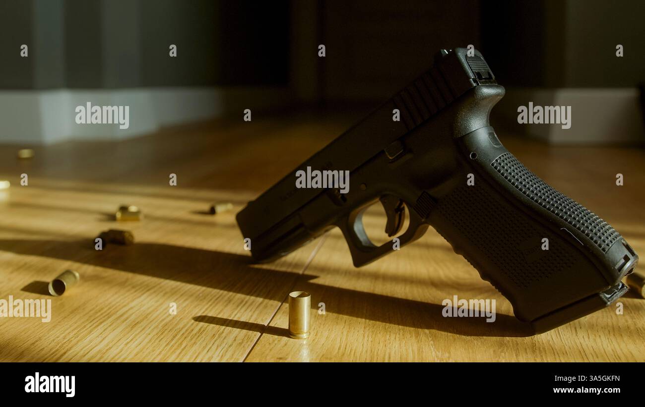 Pistola stesa sul pavimento con un involucro proiettile che cade - scenografia drammatica del crimine con illuminazione cinematografica - tensione e mistero Foto Stock