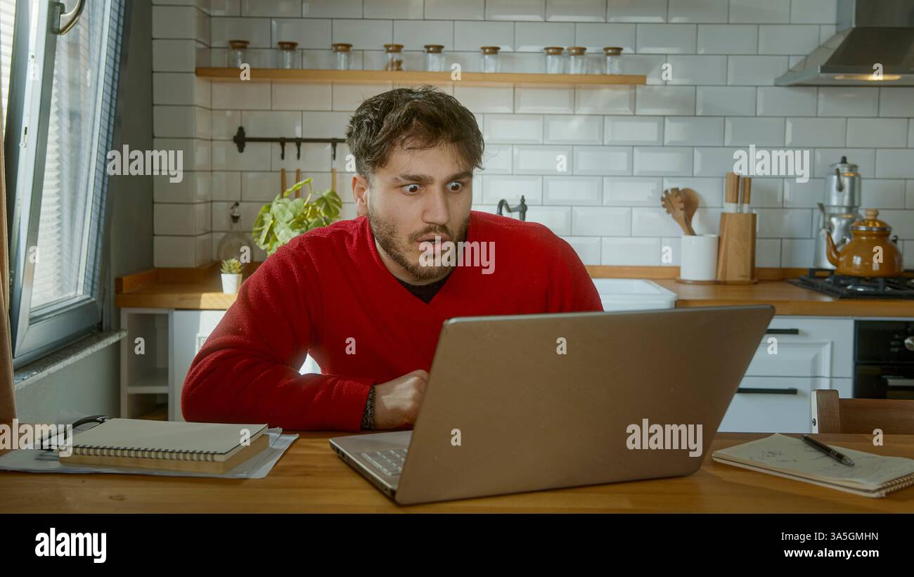 Uomo scioccato che guarda lo schermo di un notebook in una cucina moderna Foto Stock