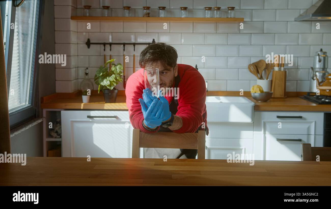 L'uomo in una cucina moderna sembra insoddisfatto di un bicchiere lavato dalla lavastoviglie, ispezionandolo da vicino con un'espressione delusa Foto Stock