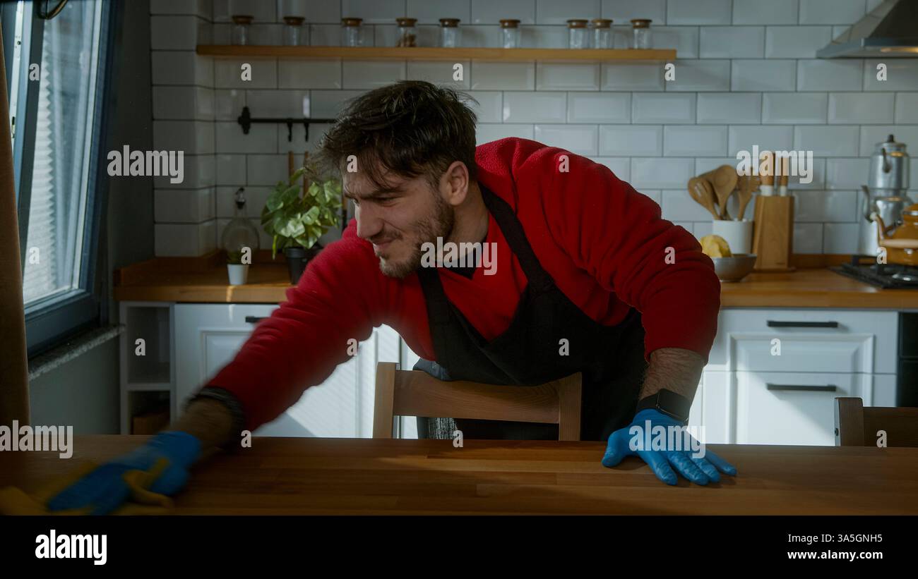 Uomo che lotta mentre pulisce la cucina, si sente esausto per le faccende domestiche Foto Stock