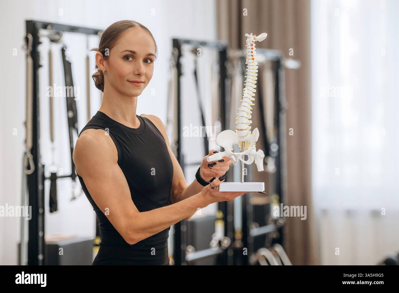 Mostra le ossa del modello della colonna vertebrale. La giovane donna è in palestra con attrezzature per l'allenamento. Foto Stock
