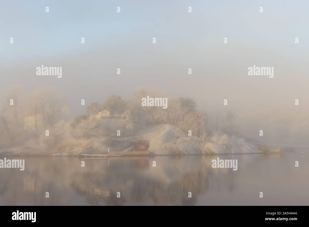 Calmo mare nebbia e gelo alla luce del mattino presto. Capanna e casa sulla spiaggia rossa. Vita sull'isola. Foto Stock