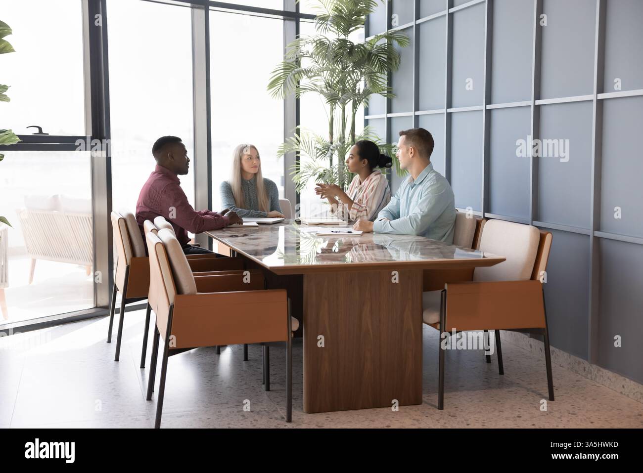 Gruppo di quattro professionisti impegnati in riunioni nella sala conferenze. Giovane donna africana capo, team leader fornisce spiegazioni, obiettivi aziendali e pubbliche relazioni Foto Stock