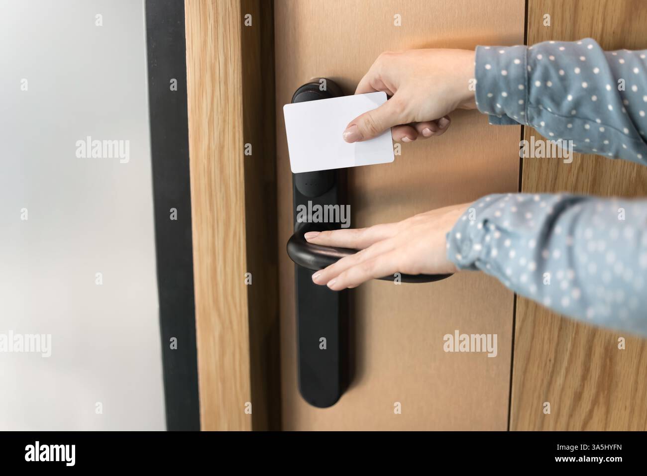 Primo piano di mani femminili sconosciute che toccano la maniglia, tieni la tessera bianca, apri la porta dell'hotel o dell'ufficio. Donna irriconoscibile che usa la chiave per accedere Foto Stock