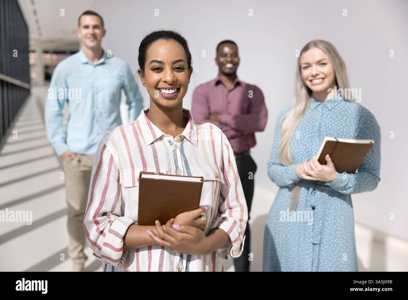 Team che posa per la fotocamera guidato da una donna africana leader o capo in piedi insieme in un moderno corridoio dell'ufficio. Membri del personale aziendale Foto Stock