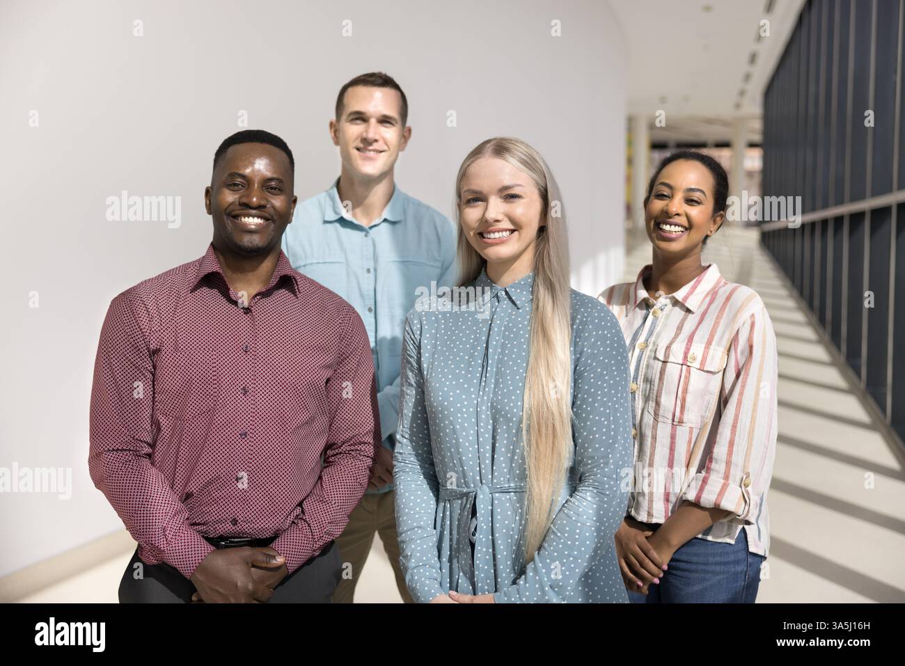 Ritratto dell'ufficio di quattro giovani team multinazionali in posa per la fotocamera in fila nel corridoio dello spazio di lavoro aziendale, trasuda professionalità. S Foto Stock