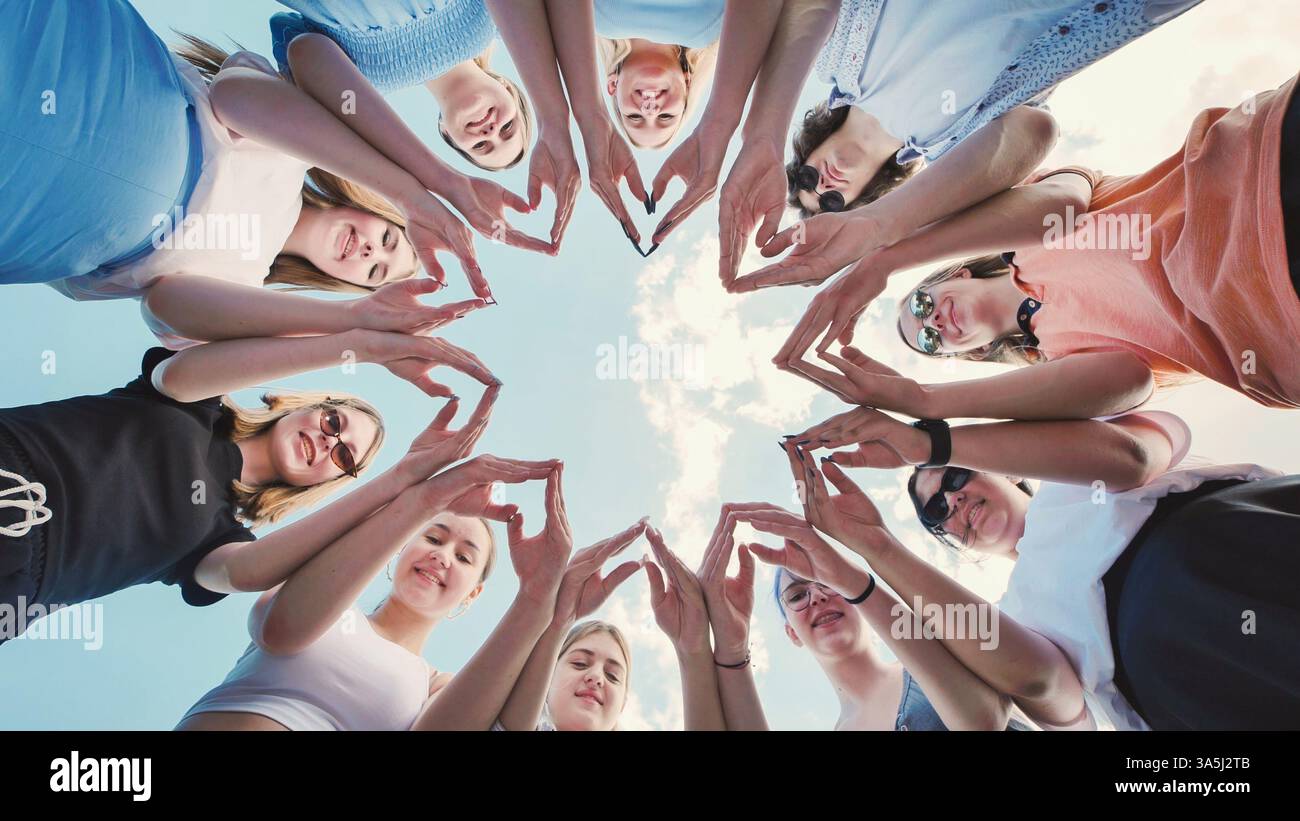 Gruppo di amici di scuola che formano una stella con le loro mani, simboleggiando l'unità, il lavoro di squadra e l'amicizia contro un cielo luminoso Foto Stock