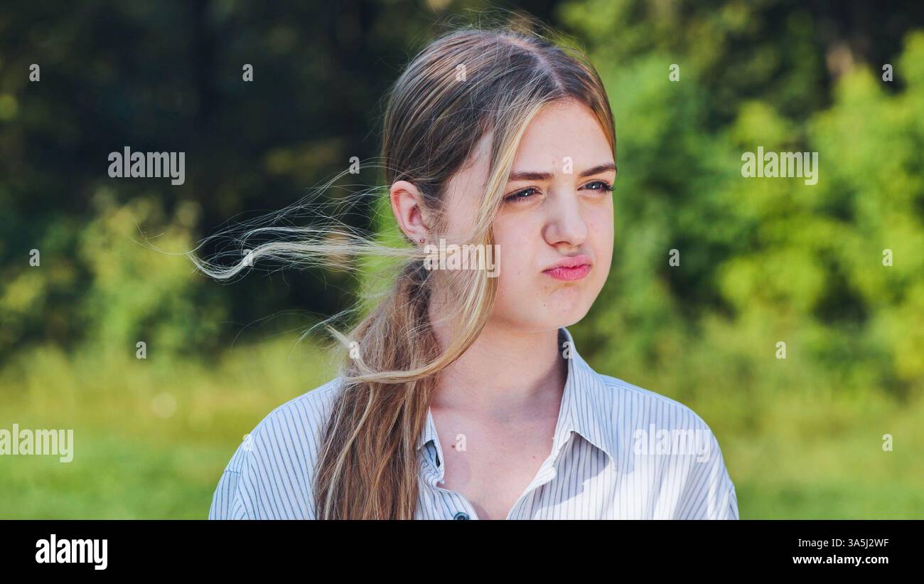 Una giovane donna scontenta con i capelli agitati in un parco, che esprime irritazione o disapprovazione in un ritratto Foto Stock