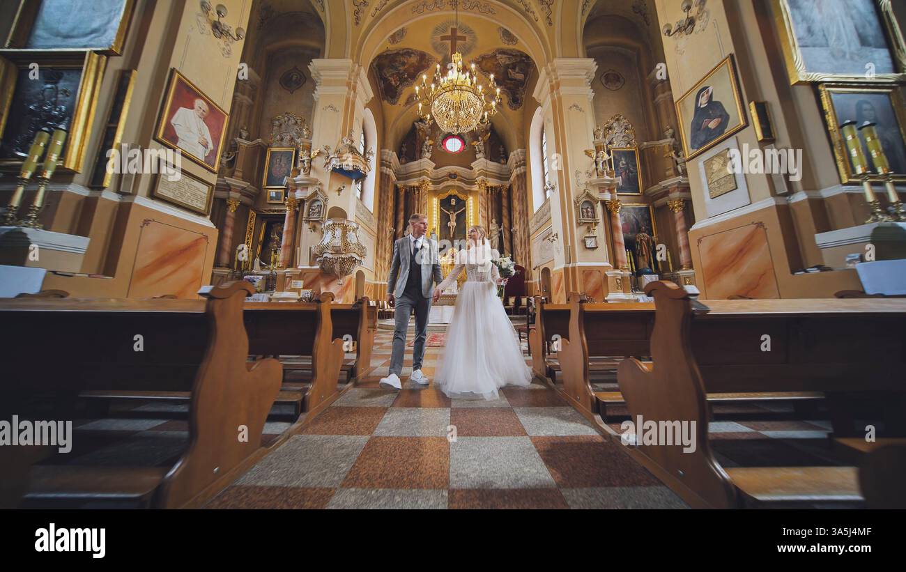Gli sposi si tengono per mano, camminano lungo la navata di una chiesa dopo la cerimonia di nozze, cominciando la loro nuova vita insieme Foto Stock