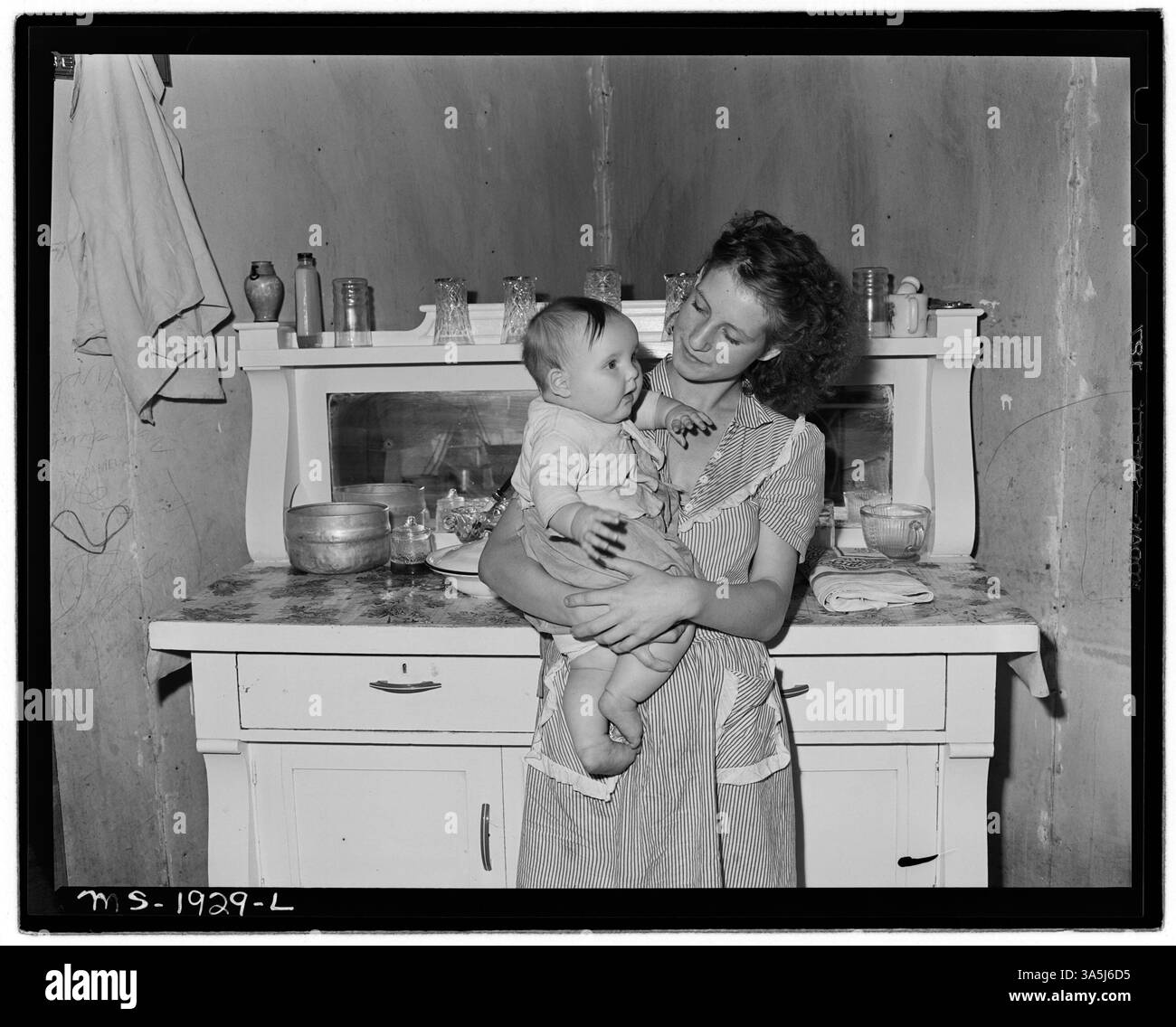 La signora Lincoln Hagg si trova nella cucina di casa sua con il bambino. Questa immagine riflette la vita in una comunità mineraria nella contea di McDowell, West Virginia, presso la miniera Douglas della Panther Red Ash Coal Corporation. Fa parte della collezione National Archives. Foto Stock