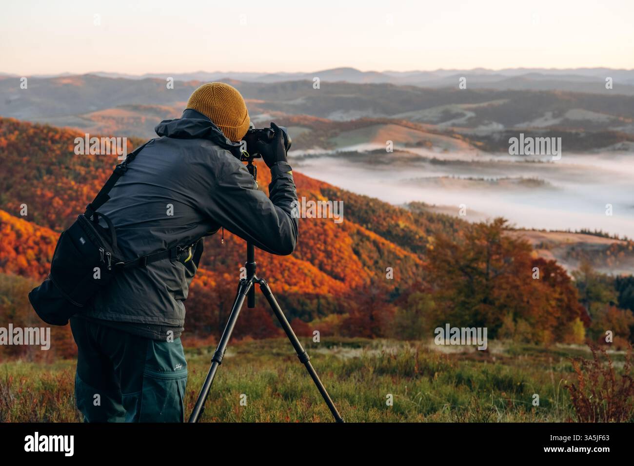 Un fotografo professionista è in piedi con la fotocamera sul treppiede e scatta una vista maestosa delle montagne dei Carpazi. Foto Stock