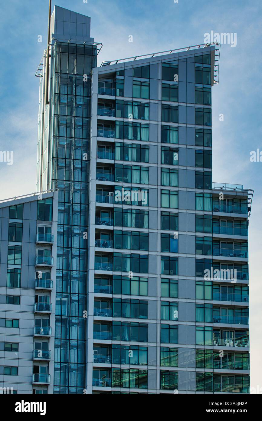 Un alto edificio con molte finestre e piccoli balconi si erge su un cielo blu con alcune nuvole a Manchester, Regno Unito. Foto Stock