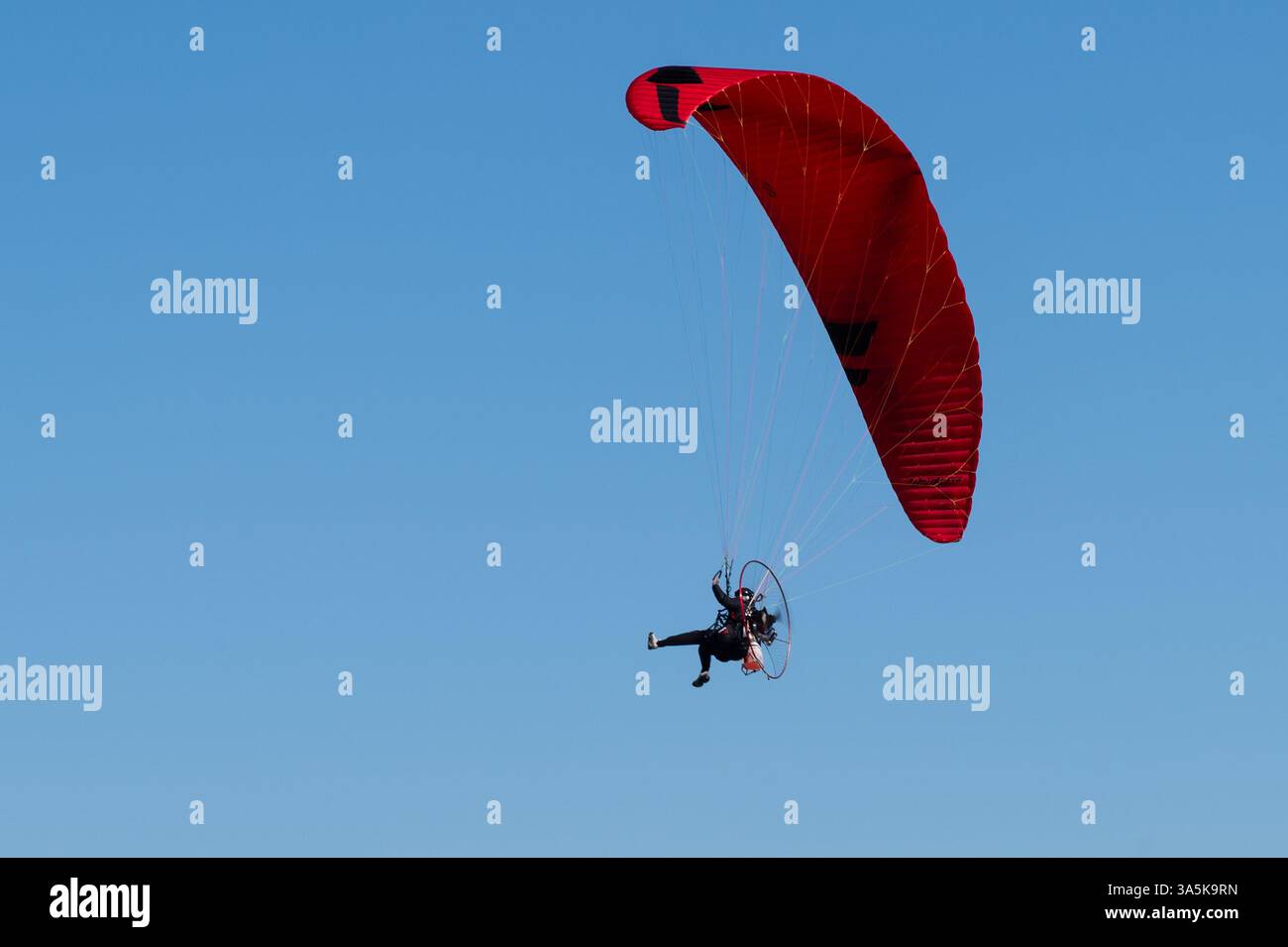 Un parapendio rosso brillante o paramotore contro un cielo blu nel Sussex, Inghilterra Foto Stock