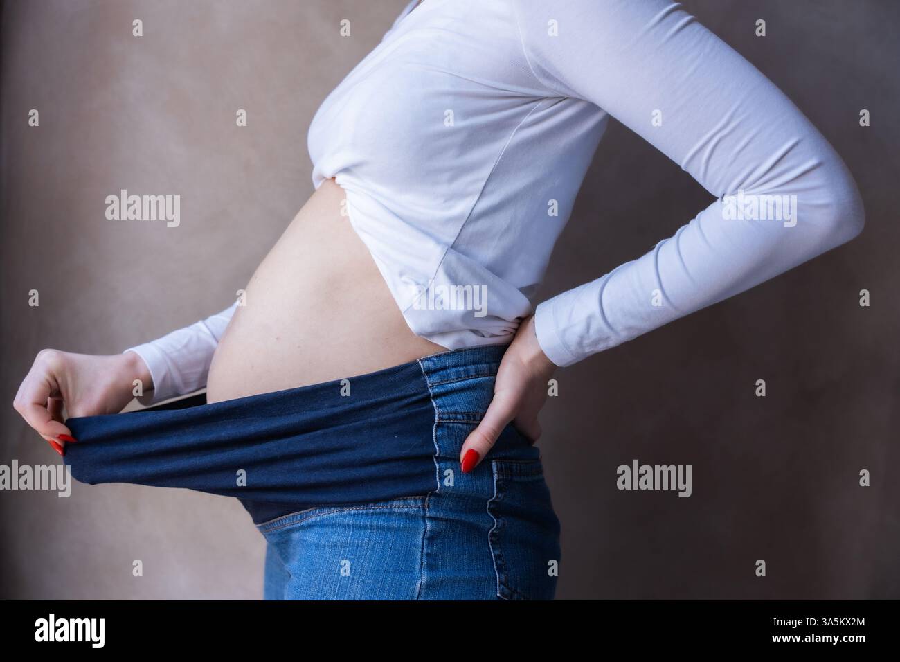 Donna incinta con pantaloni elastici per la maternità per il comfort della sua pancia Foto Stock