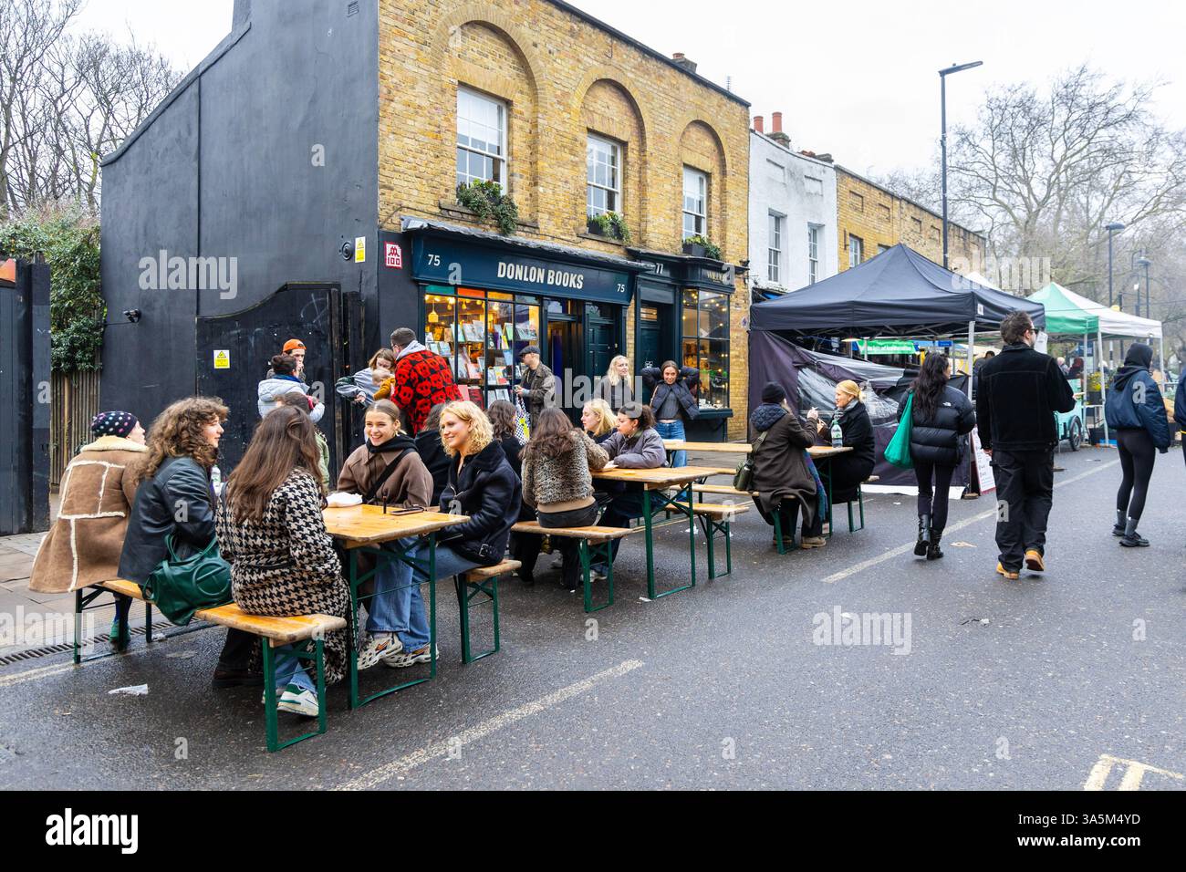 Persone sedute e mangiate ai tavoli all'aperto al Broadway Market, Hackney, Londra, Inghilterra Foto Stock
